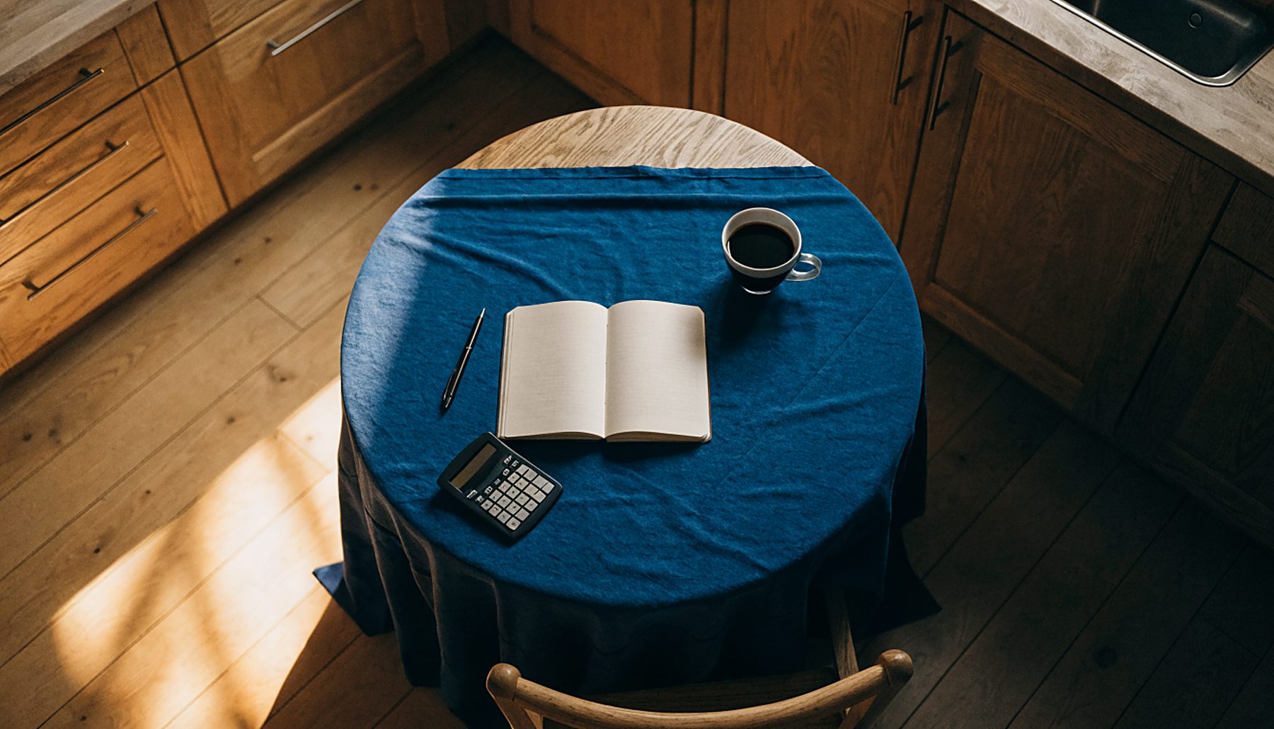 A notebook, calculator and coffee on a kitchen table, ready for a money check-in