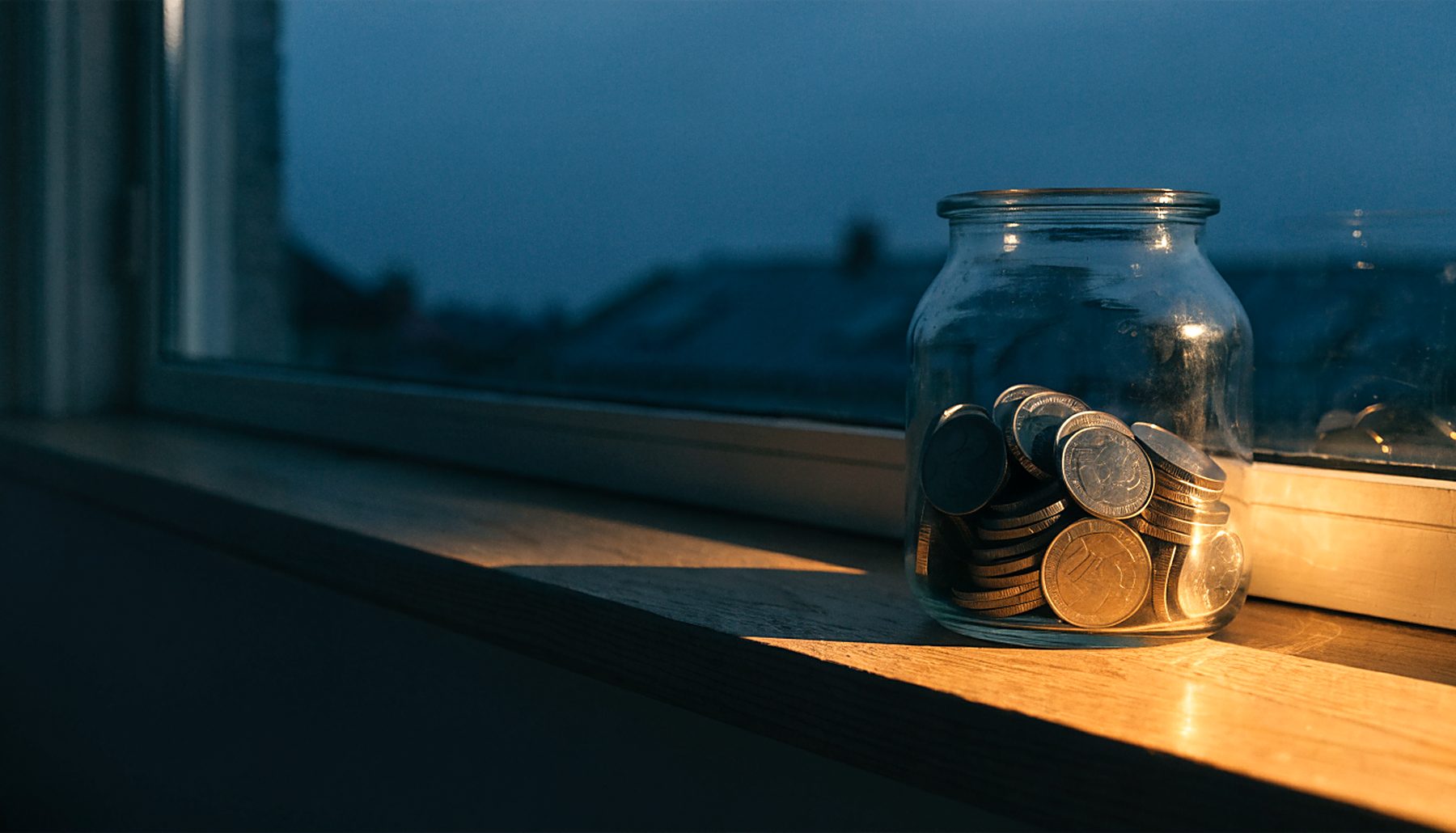 A jar of savings on a windowsill, growing coin by coin